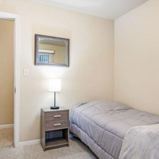 A minimalist bedroom featuring a single bed, nightstand with a lamp, and a wall-mounted mirror.