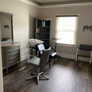 A cozy salon room with chairs, a mirror, and shelves by a window.