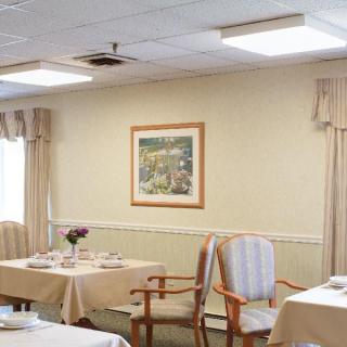 A neatly arranged dining room with tables and chairs, featuring a framed painting on the wall and elegant curtains.