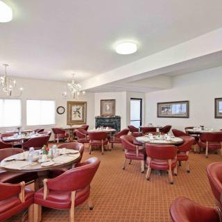 A spacious dining area featuring red leather chairs, round tables, and elegant chandeliers.