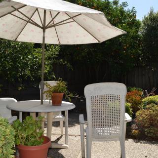 A sunny patio with a white table and chairs beneath a large umbrella, surrounded by potted plants.
