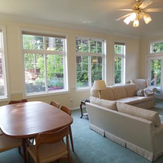 A spacious living and dining area with large windows, a ceiling fan, and comfortable furniture.