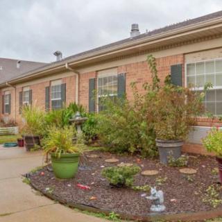 A brick house with a well-maintained garden and patio area under a cloudy sky.