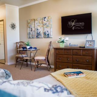 A cozy bedroom with elegant decor, featuring a television, small dining area, and wall art.