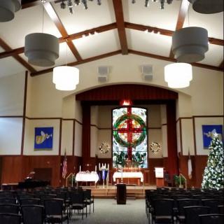 Interior of a church decorated for Christmas with a view of the altar and stained glass window.