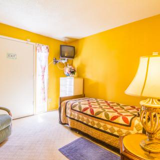 A cozy, brightly colored bedroom with a single bed, lamp, and mounted television.
