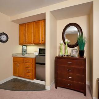 A cozy kitchenette area with wooden cabinets next to a dresser adorned with a decorative mirror and ornaments.