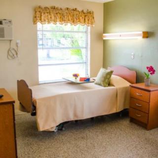 A hospital room featuring a single bed, nightstand, and window with floral curtains.