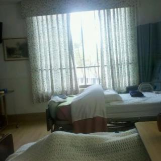 A hospital room with beds and a bright window.