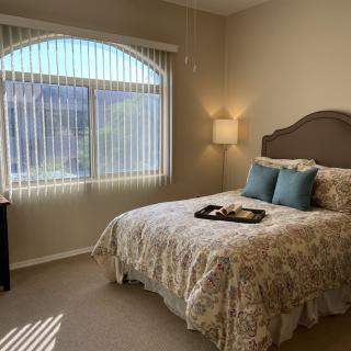 A cozy bedroom featuring a bed with patterned bedding, pillows, and abundant natural light through a large window.