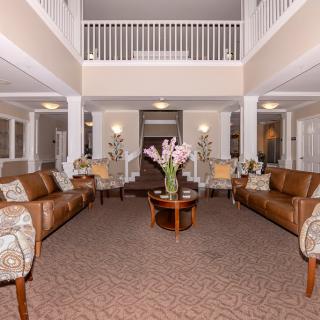 A spacious and elegantly designed lobby featuring comfortable sofas, a central coffee table with a flower arrangement, and decorative plants.