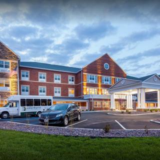 A modern hotel building with a parking lot and vehicles in the evening light.