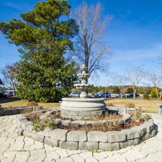 A beautifully crafted fountain surrounded by greenery and a clear blue sky.