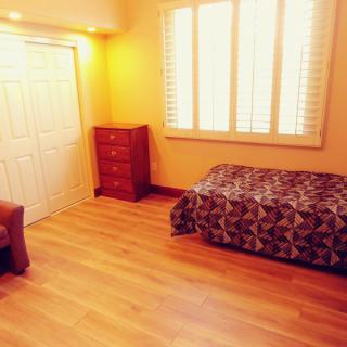 A cozy bedroom with wooden flooring, featuring a single bed, a dresser, and a window with shutters.