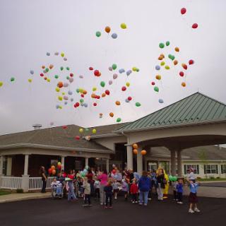 A joyful gathering of children releasing colorful balloons into the sky during a celebration.