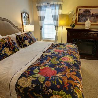 A cozy bedroom with a floral-patterned bedspread and pillows, featuring warm lighting and elegant decor.