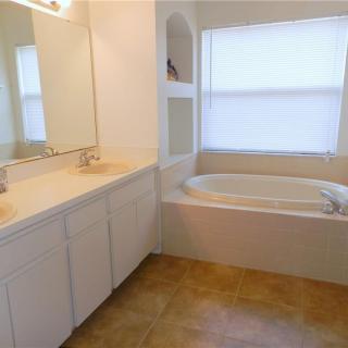 A clean and spacious bathroom with a large mirror, white cabinets, and a bathtub.