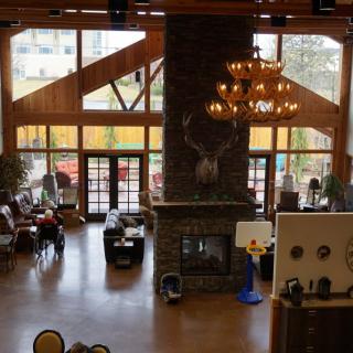 A cozy lodge interior with a central fireplace, wooden beams, and large windows.