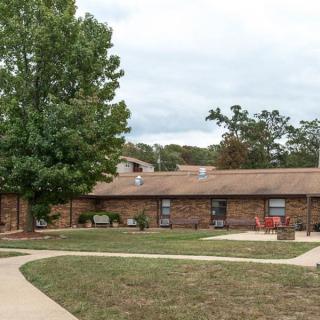 A brick residential building with a large tree and a curved pathway in the foreground.