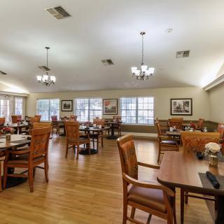 A spacious dining room with wooden tables and chairs, illuminated by chandeliers.