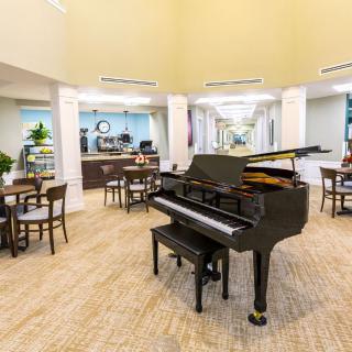 A spacious lobby featuring a grand piano surrounded by tables and chairs, with stylish decor and lighting.