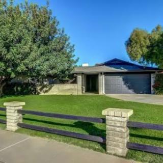 A modern single-story house featuring a well-manicured front yard with a fence and surrounding trees.