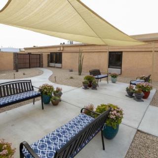 A cozy patio area with benches, shade sails, and potted plants in a desert landscape.