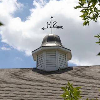 A rooftop cupola with a weathervane pointing directions against a cloudy sky.