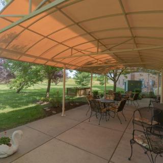A cozy patio with an awning providing shade over tables and chairs, overlooking a lush garden.