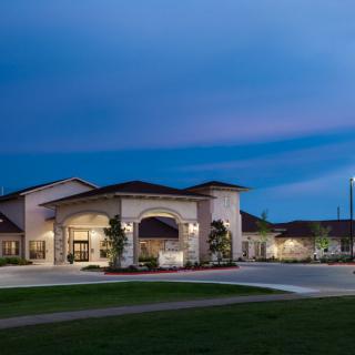 A well-lit building with an arched entrance at dusk, surrounded by open green space.