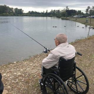 A senior person in a wheelchair fishing by a lake.