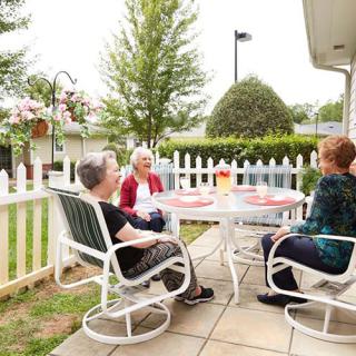 A group of seniors enjoying a conversation on a patio surrounded by a garden.