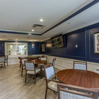 A spacious and elegant dining area with blue walls, featuring multiple tables and chairs, a TV mounted on the wall, and wood flooring.