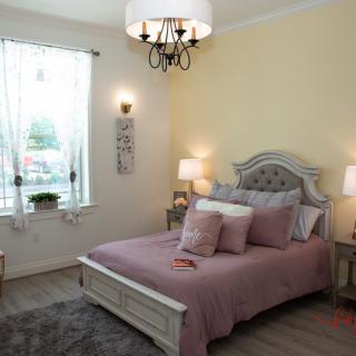 A cozy bedroom featuring a comfortable bed with pastel bedding, a stylish chandelier, and elegant decor.