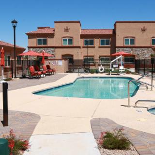 A serene outdoor swimming pool area within an apartment complex on a sunny day, featuring patio furniture and umbrellas.