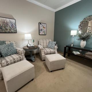 A cozy living room featuring patterned armchairs, matching ottomans, soft lighting from table lamps, and decorative wall art.