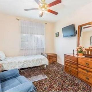 A cozy bedroom with a single bed, dresser, wall-mounted TV, and a ceiling fan.