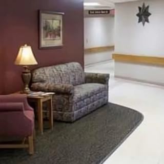 A hospital waiting area with a sofa and lamp, leading to a corridor.