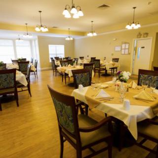 A warmly lit dining room with several set tables and chairs, featuring elegant chandeliers and a wooden floor.