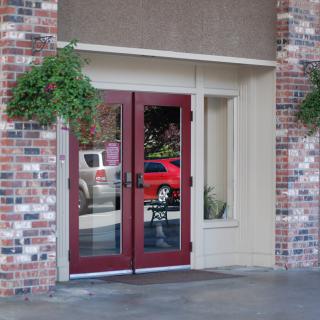 A building entrance with red glass doors, surrounded by a brick wall and hanging plants.