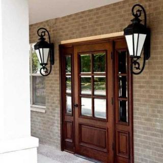 A wooden entrance door flanked by decorative lanterns on a brick wall.