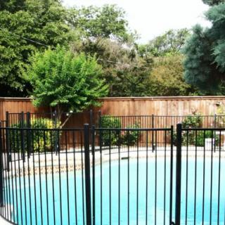 A swimming pool surrounded by a safety fence and lush greenery.