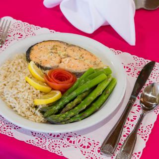 A plate of salmon served with rice, asparagus, and lemon slices on a neatly arranged table setting.