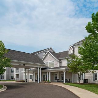 A large residential building with a driveway and trees under a partly cloudy sky.