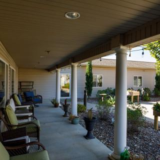 A covered porch with seating and landscaping, featuring columns and a garden area.