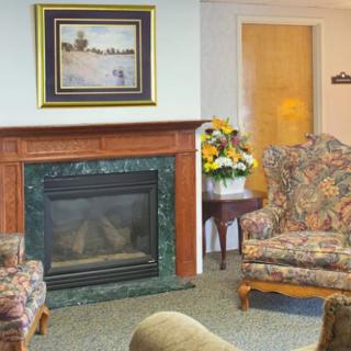 A cozy living room with a decorative fireplace, floral armchairs, and a landscape painting above the mantel.