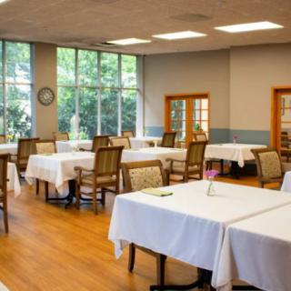 A spacious dining room with neatly arranged tables and chairs, featuring large windows and elegant table settings.