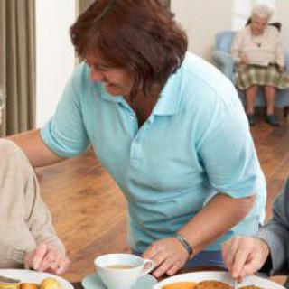 A caregiver assists elderly residents during a meal in an assisted living facility.