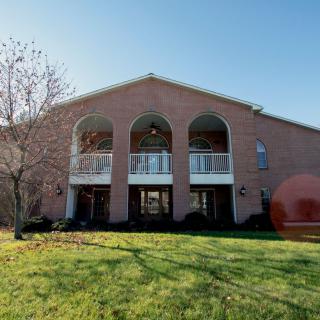 A two-story brick house with arches and balconies, surrounded by a grassy lawn.