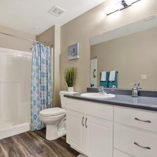 A modern bathroom featuring a sink with a large mirror, a shower with a blue curtain, and neatly arranged towels.